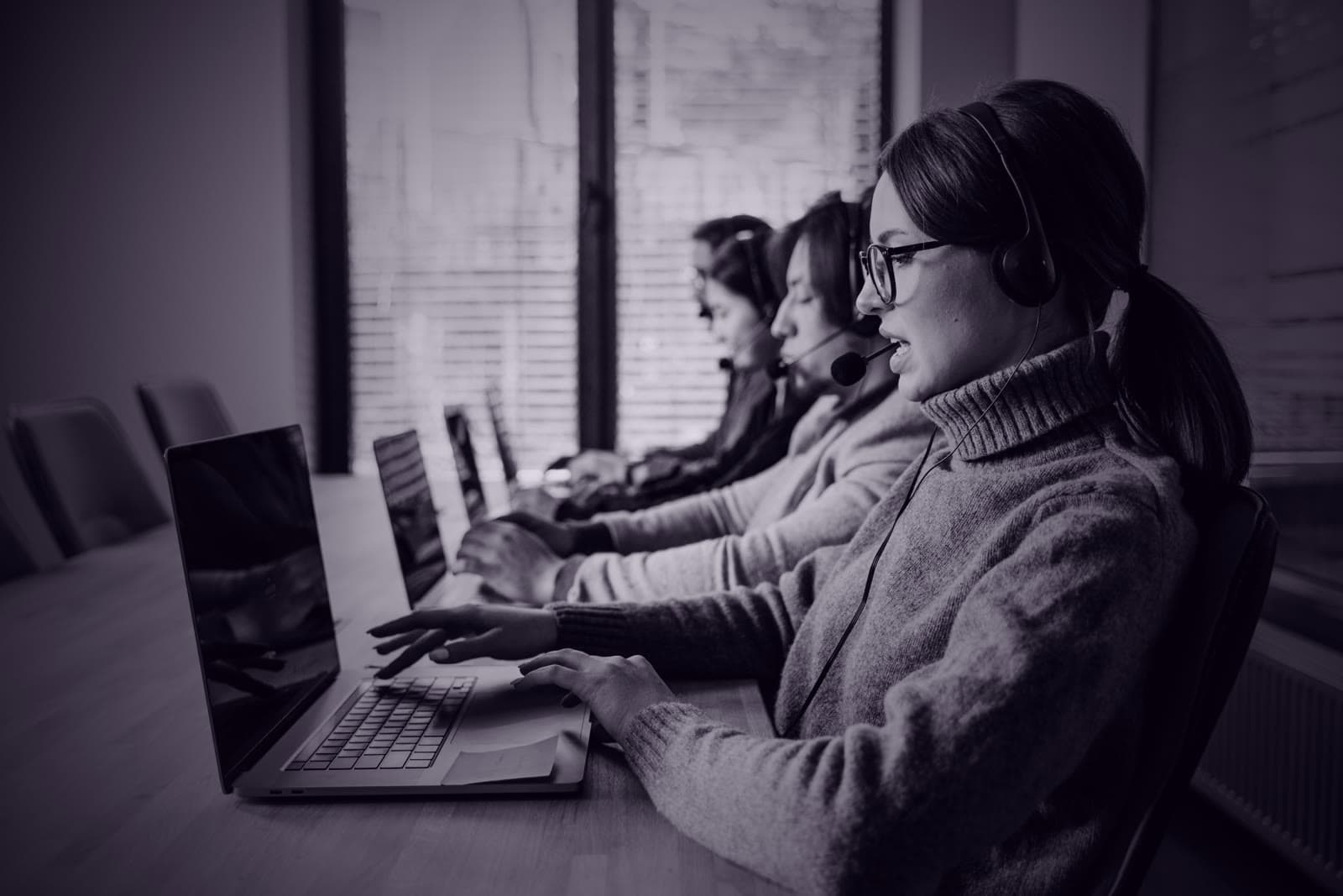 A BDC agent in glasses on a headset answering leads, with her teammates working along the desk behind her